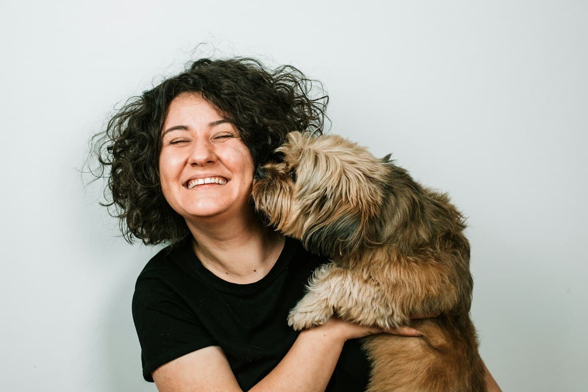 A laughing woman cuddling her fluffy dog as it nuzzles her face